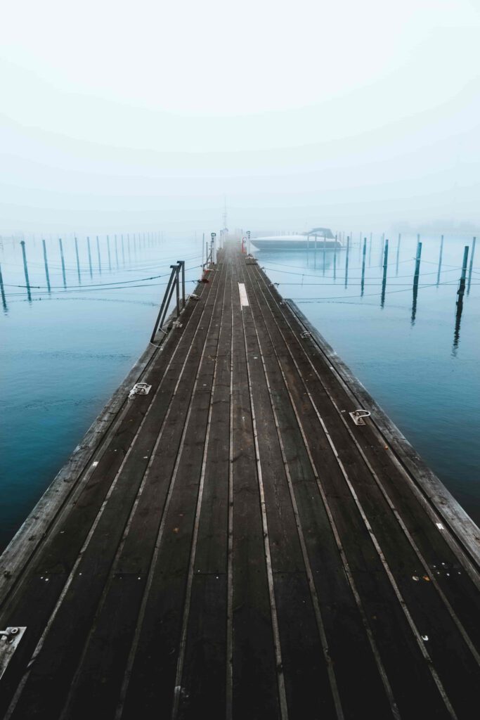 En tom brygga i Varbergs småbåtshamn på en dimmig vintermorgon i december, med frosttäckt trädäck och stilla, gråblått vatten under en blek himmel.